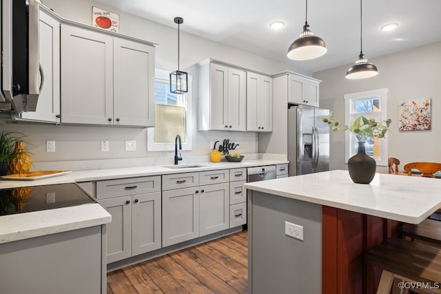 kitchen featuring a breakfast bar, gray cabinets, stainless steel appliances, pendant lighting, and a sink