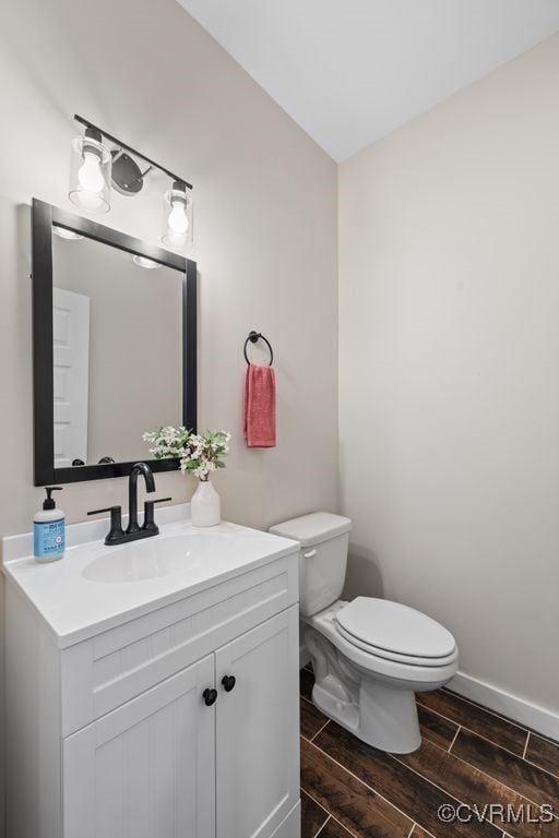 half bath featuring toilet, wood tiled floor, baseboards, and vanity