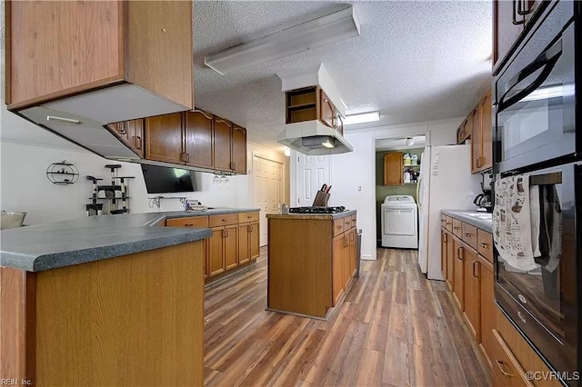 kitchen featuring a kitchen island, a peninsula, washer / clothes dryer, a textured ceiling, and light wood-type flooring