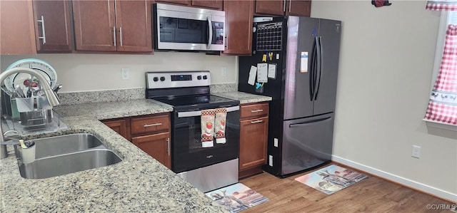 kitchen with light stone counters, stainless steel appliances, light wood-style flooring, a sink, and baseboards