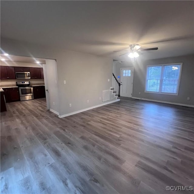 unfurnished living room with wood finished floors, visible vents, baseboards, and stairs