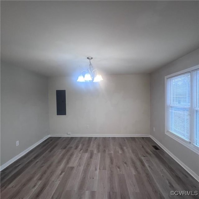 spare room featuring a healthy amount of sunlight, electric panel, baseboards, and a notable chandelier