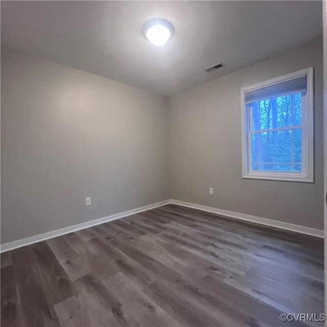 empty room featuring dark wood-type flooring, visible vents, and baseboards