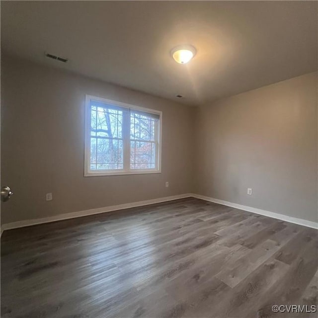 unfurnished room with dark wood-type flooring, visible vents, and baseboards