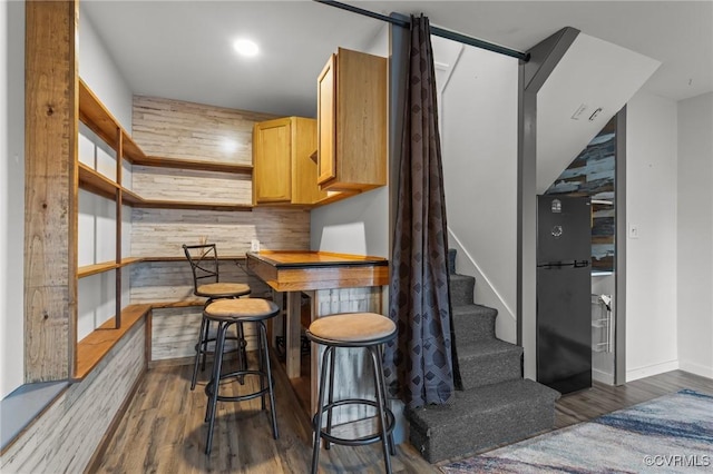 bar featuring stairs, wood finished floors, freestanding refrigerator, and wooden walls