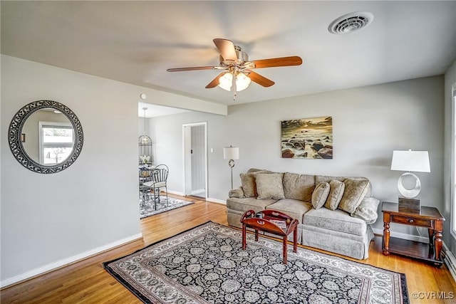 living room featuring baseboards, ceiling fan, visible vents, and wood finished floors