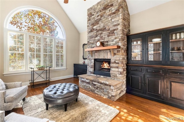 living room with high vaulted ceiling, wood finished floors, a fireplace, baseboards, and ceiling fan