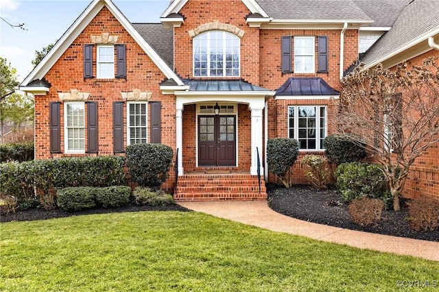 view of front of home featuring a shingled roof, metal roof, a standing seam roof, a front yard, and brick siding