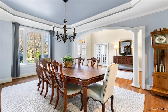 dining room featuring arched walkways, crown molding, a tray ceiling, and wood finished floors