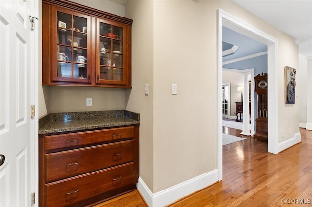 hallway with decorative columns, light wood-style floors, baseboards, and ornamental molding