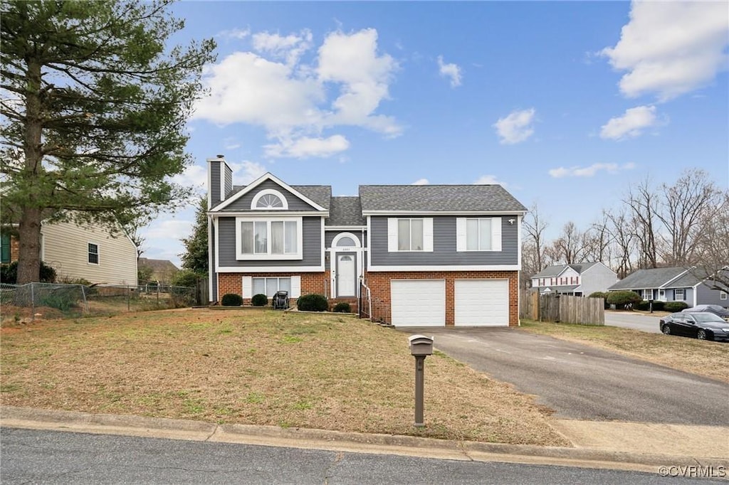 split foyer home featuring driveway, a chimney, an attached garage, fence, and brick siding