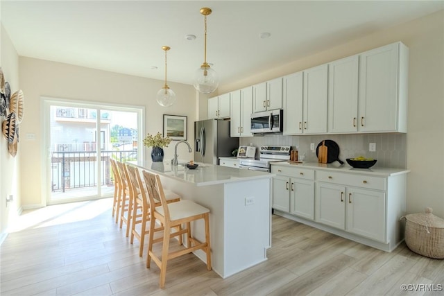 kitchen with a kitchen island with sink, white cabinetry, light countertops, appliances with stainless steel finishes, and pendant lighting