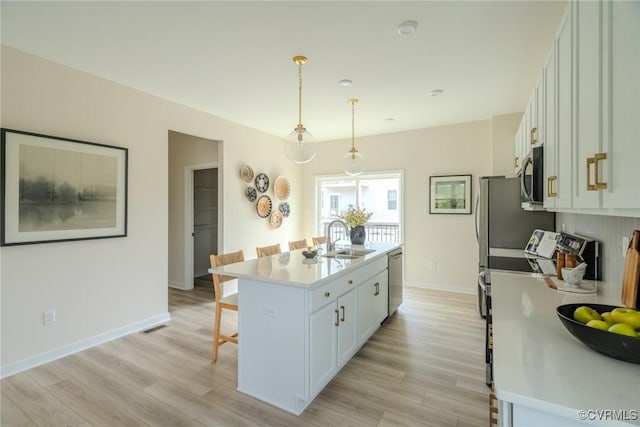 kitchen with a breakfast bar area, a sink, white cabinets, an island with sink, and decorative light fixtures