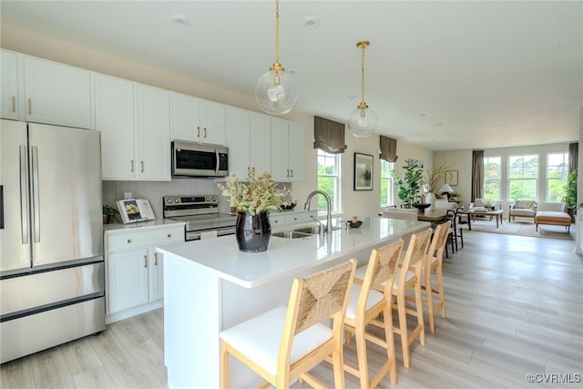 kitchen featuring an island with sink, appliances with stainless steel finishes, a breakfast bar area, light countertops, and pendant lighting