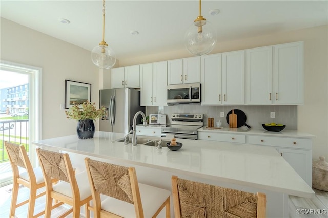 kitchen featuring white cabinets, appliances with stainless steel finishes, hanging light fixtures, light countertops, and a sink