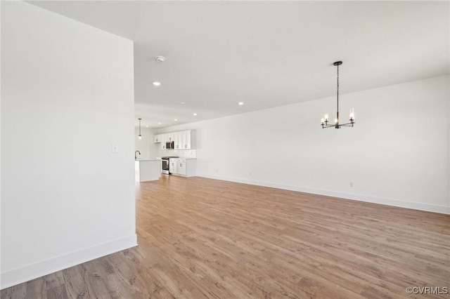 unfurnished living room with a notable chandelier, light wood finished floors, recessed lighting, a sink, and baseboards