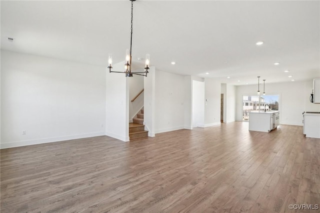 unfurnished living room with recessed lighting, a sink, baseboards, stairs, and light wood-style floors