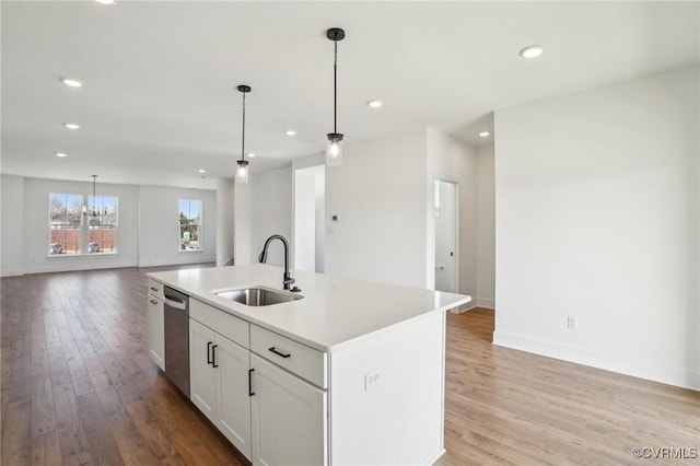 kitchen featuring an island with sink, open floor plan, a sink, light countertops, and stainless steel dishwasher