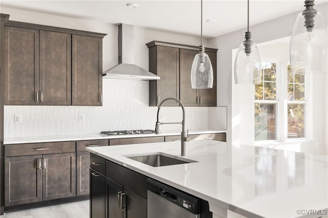 kitchen featuring decorative light fixtures, backsplash, appliances with stainless steel finishes, a sink, and wall chimney range hood