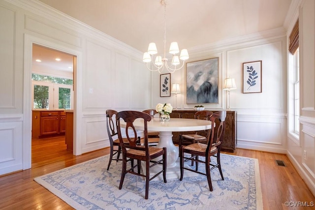 dining space with light wood-type flooring, visible vents, a decorative wall, and a chandelier