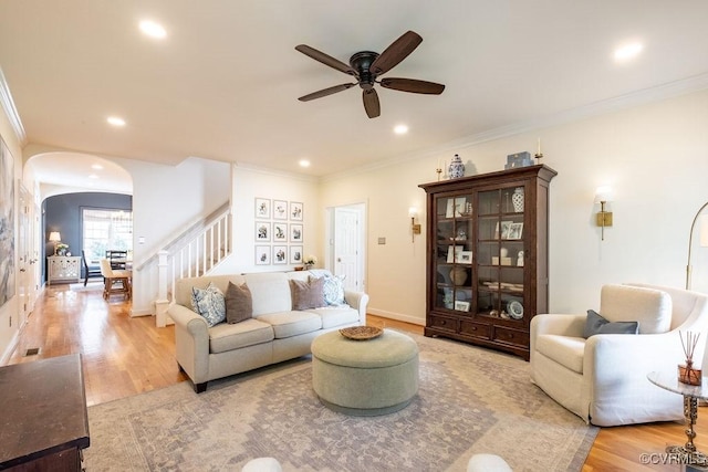 living room with arched walkways, light wood-style flooring, ornamental molding, stairs, and recessed lighting