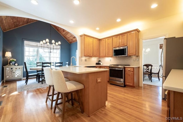 kitchen with lofted ceiling, a breakfast bar area, an inviting chandelier, stainless steel appliances, and a sink