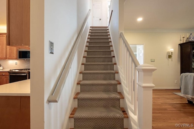 staircase featuring baseboards, ornamental molding, wood finished floors, and recessed lighting