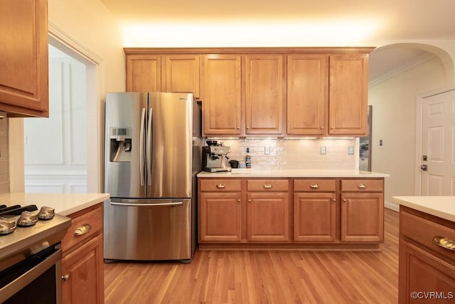 kitchen featuring arched walkways, light wood-style floors, stainless steel fridge with ice dispenser, light countertops, and decorative backsplash