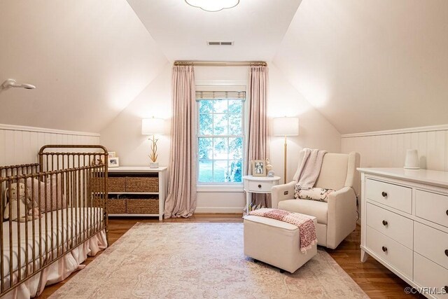 bedroom featuring vaulted ceiling, a crib, wood finished floors, and visible vents