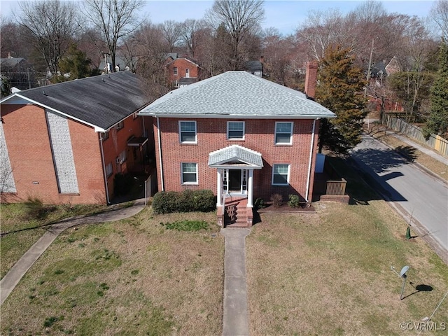 view of front of property featuring brick siding, fence, roof with shingles, a chimney, and a front yard