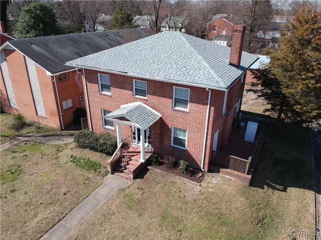 view of front of home with brick siding, a chimney, a front yard, and a shingled roof