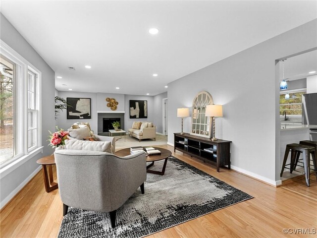 living room with baseboards, visible vents, light wood-style flooring, a fireplace, and recessed lighting