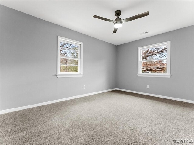 carpeted spare room featuring baseboards, visible vents, ceiling fan, and a wealth of natural light