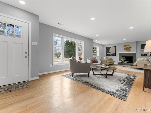 living room with baseboards, light wood-type flooring, a fireplace, and recessed lighting