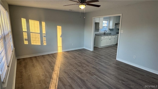 interior space featuring ceiling fan, baseboards, dark wood-style flooring, and a sink