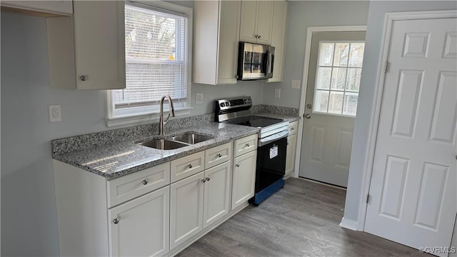 kitchen with appliances with stainless steel finishes, wood finished floors, light stone countertops, white cabinetry, and a sink