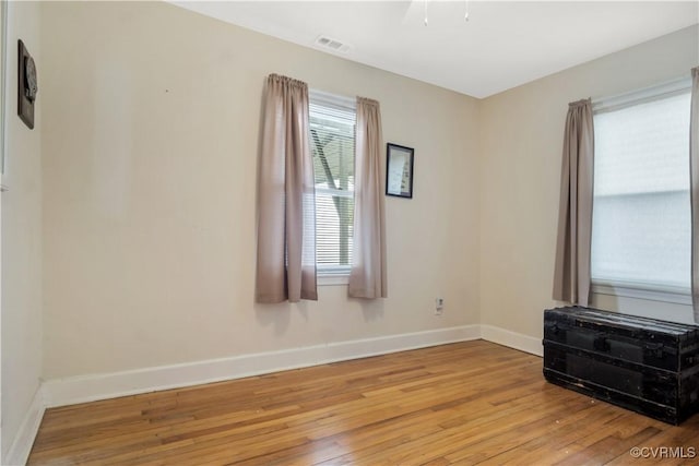 empty room with light wood-type flooring, visible vents, and baseboards