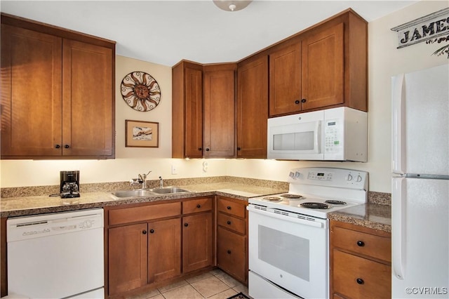 kitchen with brown cabinetry, white appliances, a sink, and light tile patterned floors