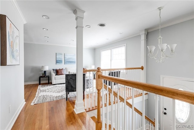 hall with a notable chandelier, wood finished floors, an upstairs landing, ornamental molding, and decorative columns