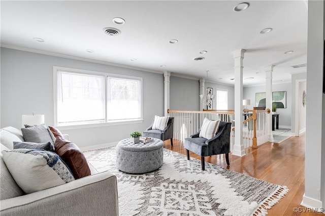 living area featuring a wealth of natural light, decorative columns, visible vents, and crown molding