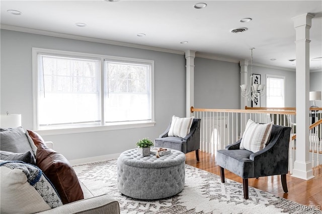 living area featuring ornate columns, visible vents, wood finished floors, and ornamental molding