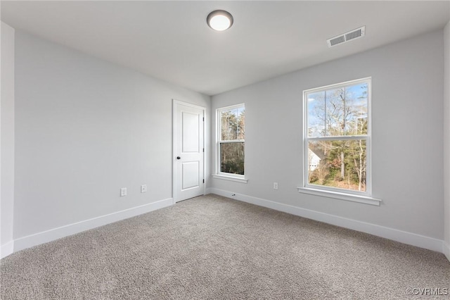 carpeted spare room featuring plenty of natural light, visible vents, and baseboards