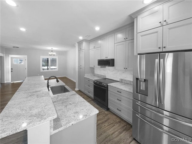 kitchen with stainless steel refrigerator with ice dispenser, black range with electric stovetop, a kitchen island with sink, a sink, and light stone countertops