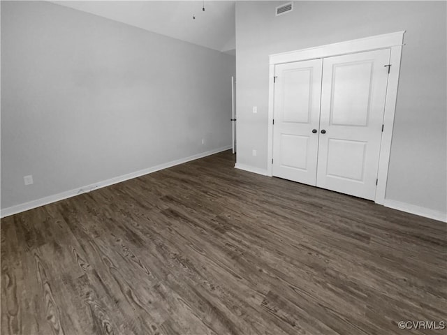 unfurnished bedroom featuring dark wood-style flooring, a closet, visible vents, vaulted ceiling, and baseboards