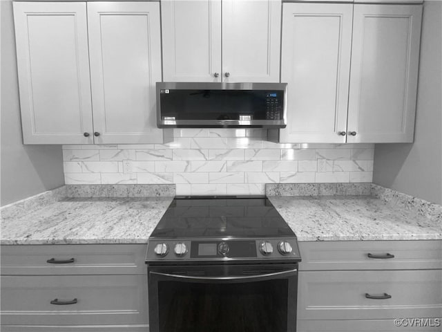 kitchen featuring stainless steel microwave, decorative backsplash, range with electric stovetop, and white cabinets