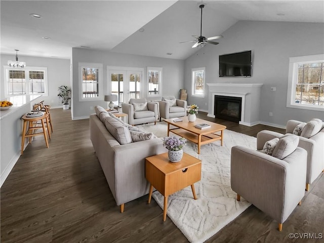 living room with a glass covered fireplace, a healthy amount of sunlight, dark wood finished floors, and lofted ceiling