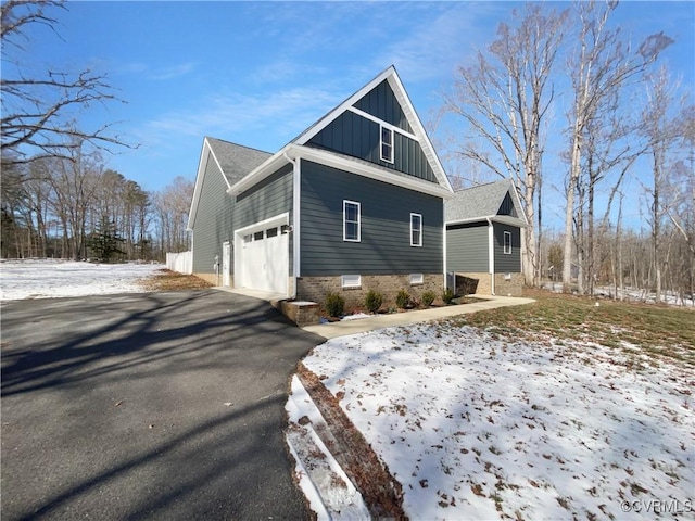 snow covered property featuring board and batten siding, driveway, and an attached garage