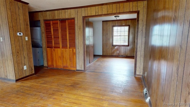 corridor featuring light wood-style floors, stacked washer / drying machine, wood walls, and baseboards