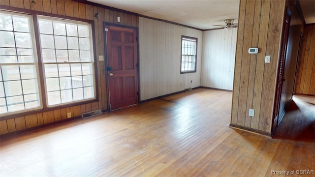 foyer entrance with a ceiling fan, baseboards, visible vents, light wood finished floors, and crown molding