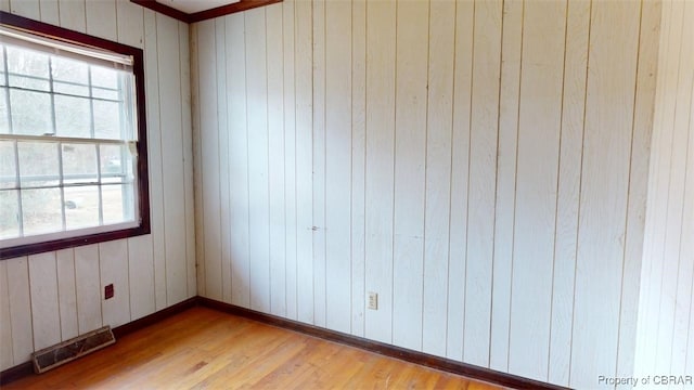 spare room featuring wood walls, wood finished floors, visible vents, and baseboards